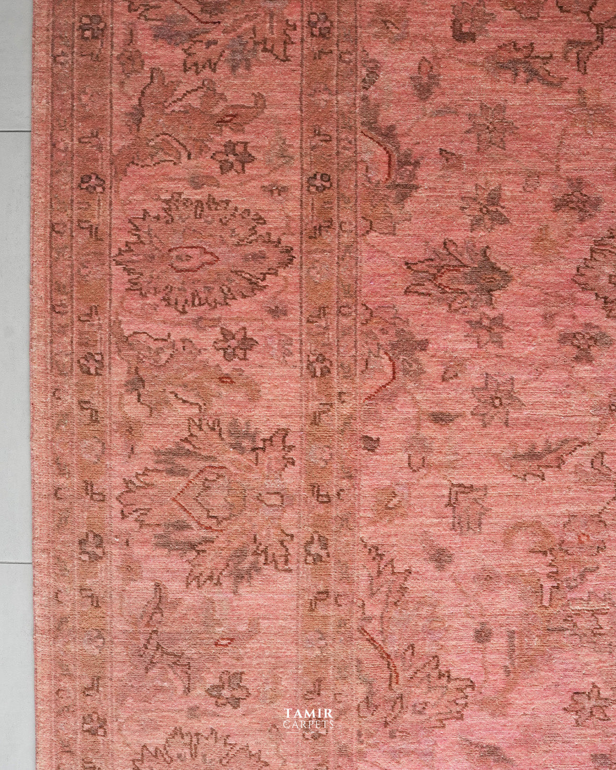 A close-up of a traditional patterned rug in dusty rose pink and brown tones, showing floral motifs and a central border.