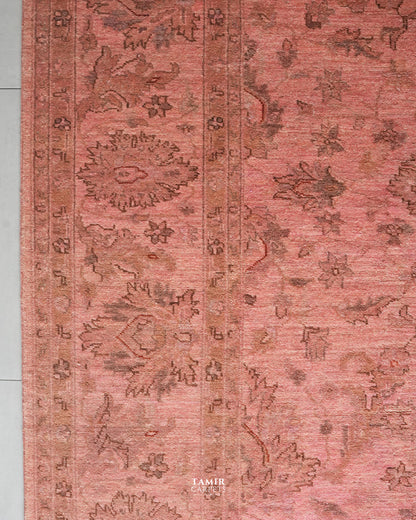 A close-up of a traditional patterned rug in dusty rose pink and brown tones, showing floral motifs and a central border.