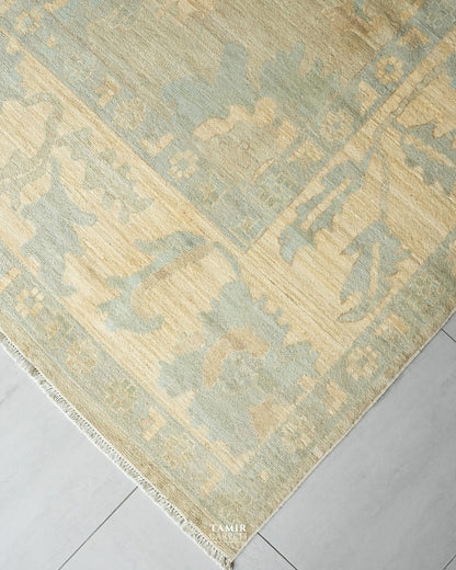 A close-up of a traditional area rug with a distressed, faded pattern in sage green and beige, laid out on a light gray tiled floor.