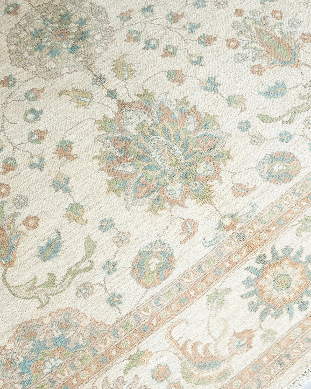 A close-up of a traditional patterned rug with an ivory base and floral motifs in muted blue, sage green, and peach.