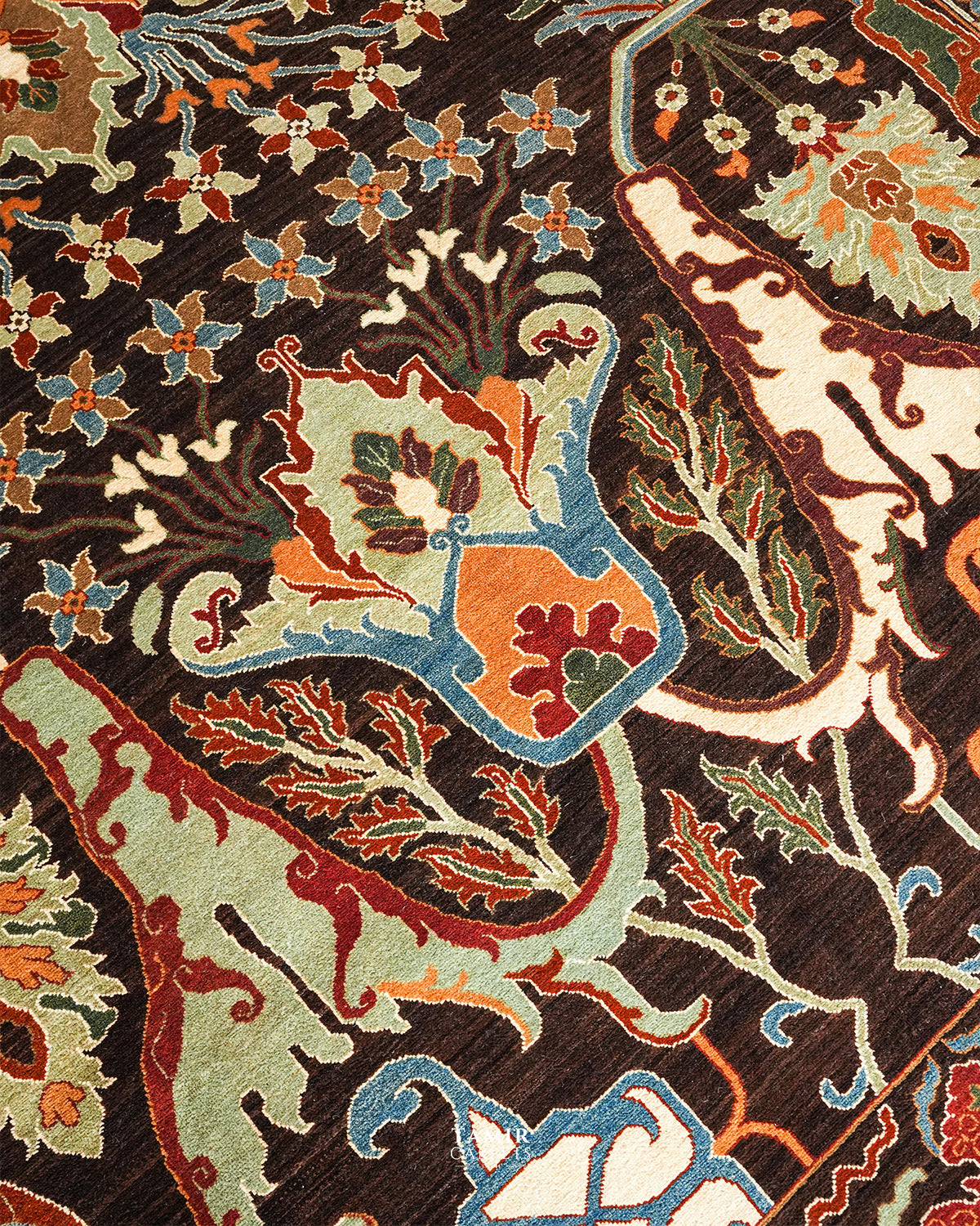 Close-up of an ornate woven rug pattern with a dark brown ground and multicolored floral and scroll motifs in cream, blue, orange, red, and green.