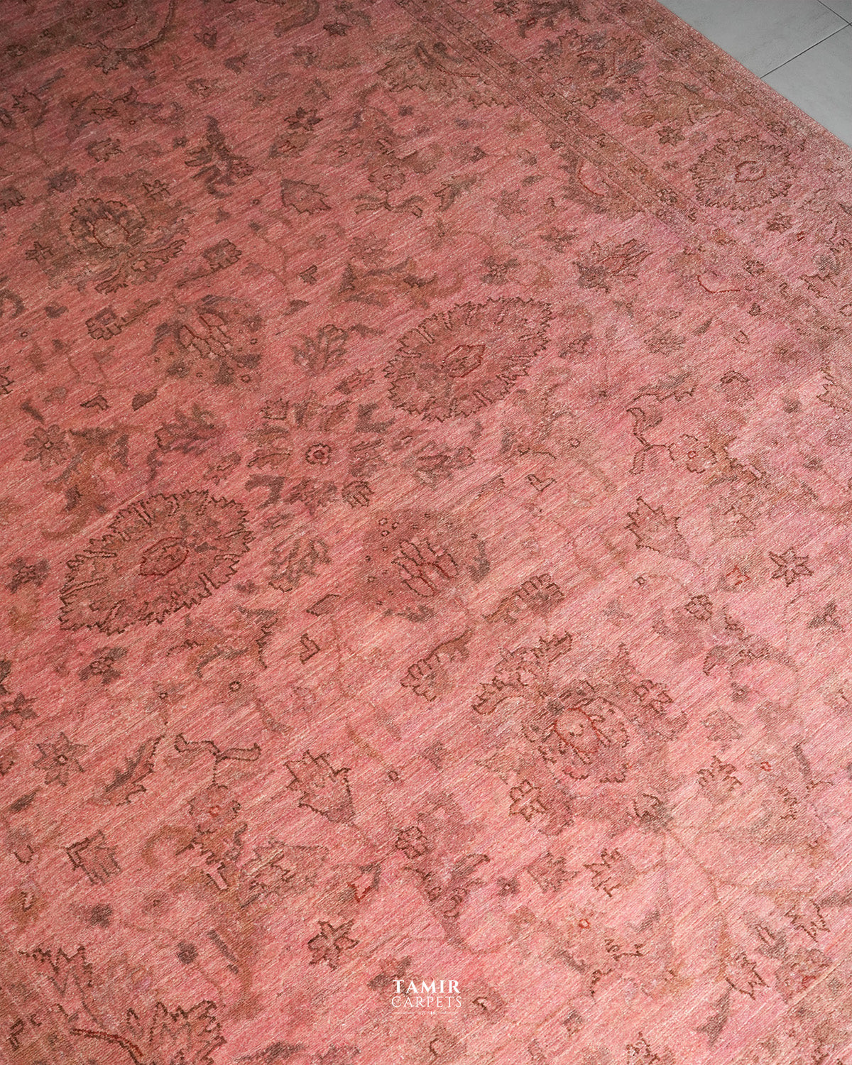 A close-up of a dusty pink area rug with a faded traditional floral and medallion pattern in muted brown tones.