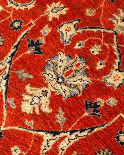 A close-up of a traditional patterned rug with a vibrant red field, featuring cream, gray, and black floral motifs.