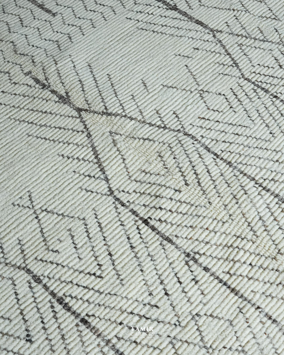 A close-up of a woven rug or textile with a geometric pattern in off-white and dark gray.