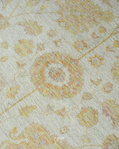 A close-up of a textured area rug featuring a traditional floral and medallion pattern in soft yellow, peach, and muted blue on a warm off-white background.