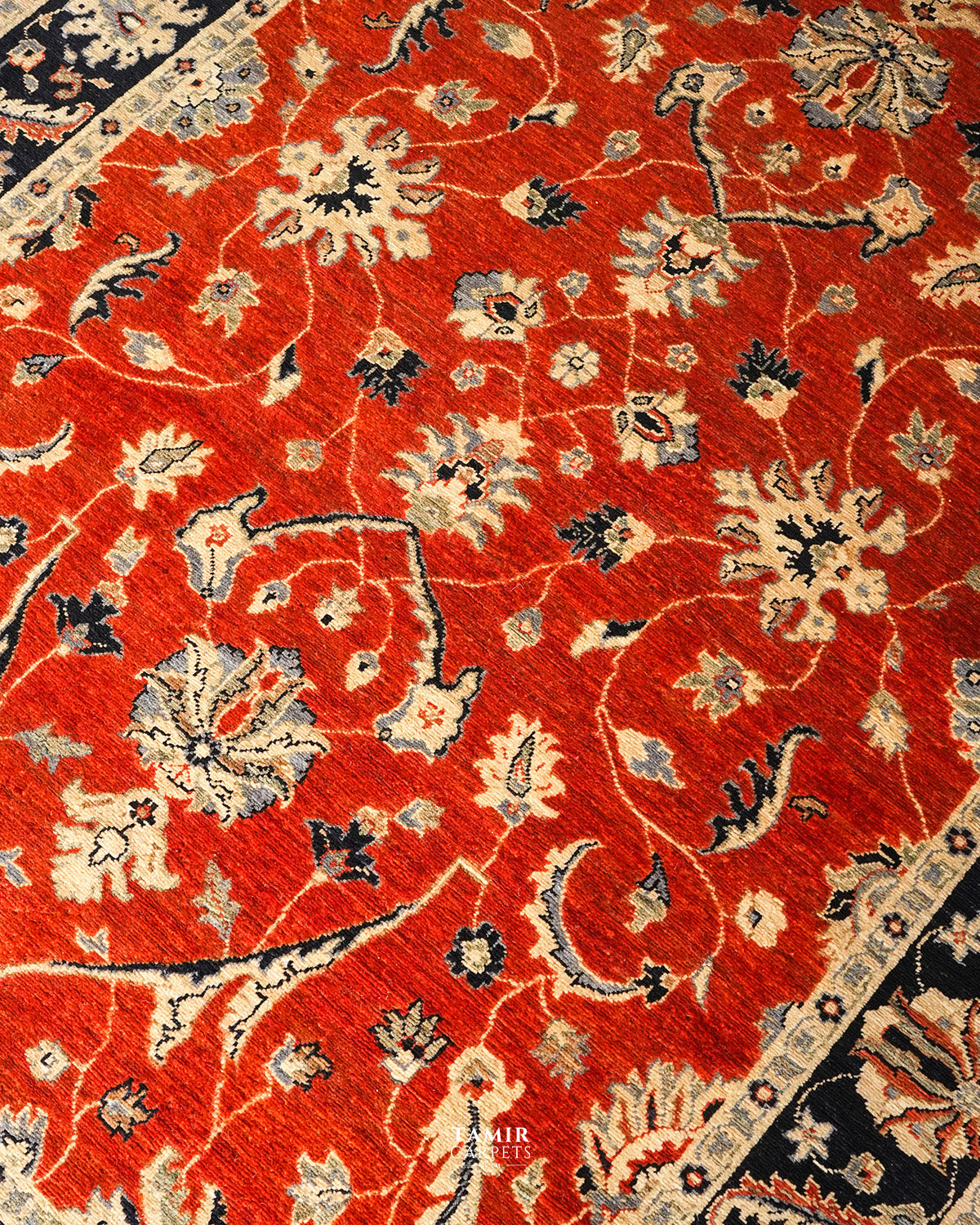 A close-up of a traditional oriental rug with a vibrant red field, featuring cream, beige, and navy blue floral and vine patterns.