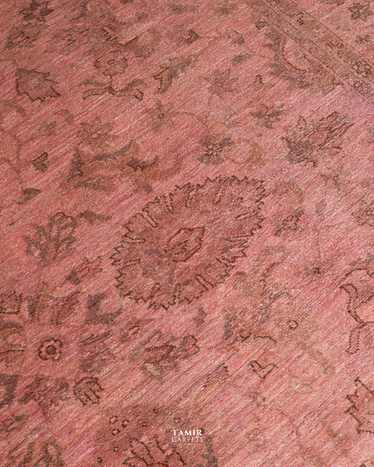 A close-up of a pinkish-red patterned rug with a traditional floral and medallion design in darker brown tones. The brand name 'TAMIR CARPETS' is visible as a watermark at the bottom center.