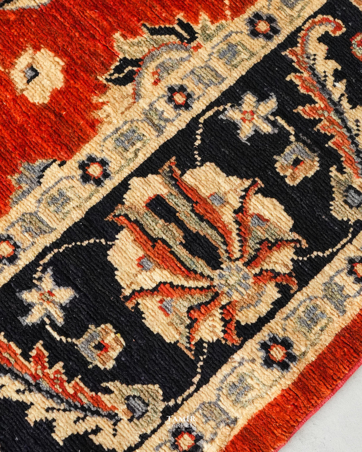 Close-up of a patterned rug showing a red field, a black central panel, and cream floral motifs with small blue-gray accents.