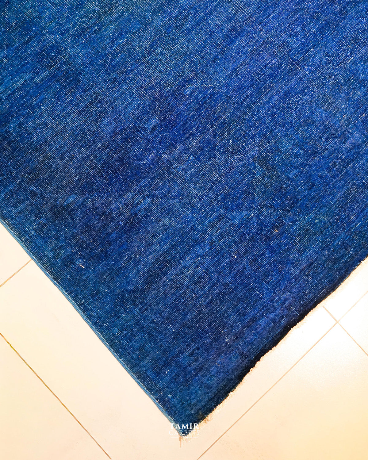 Corner of the blue overdyed Chobi rug on a tiled floor