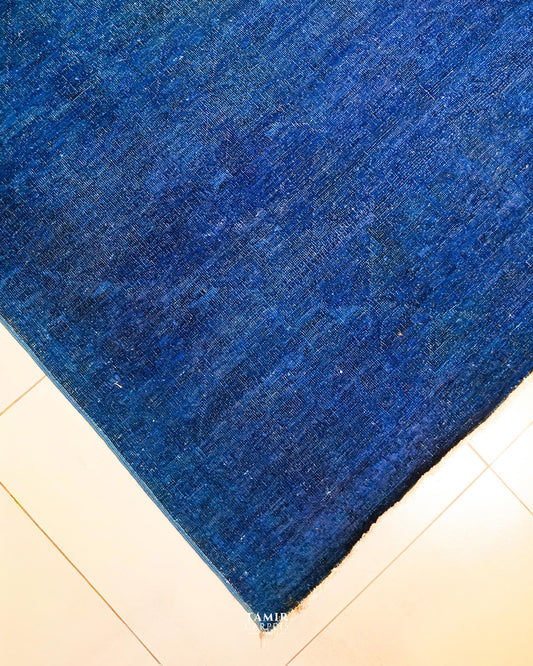 Corner of the blue overdyed Chobi rug on a tiled floor