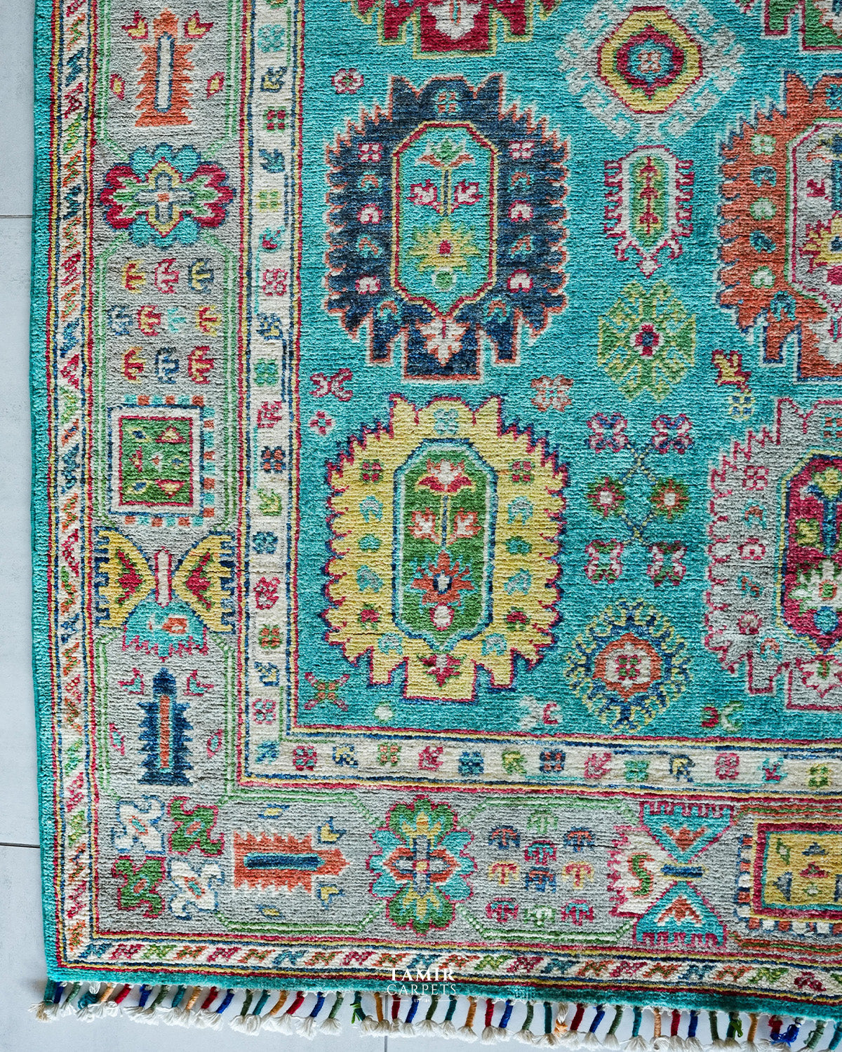 Corner of the Khurjeen rug showing the ivory border and multicoloured fringe