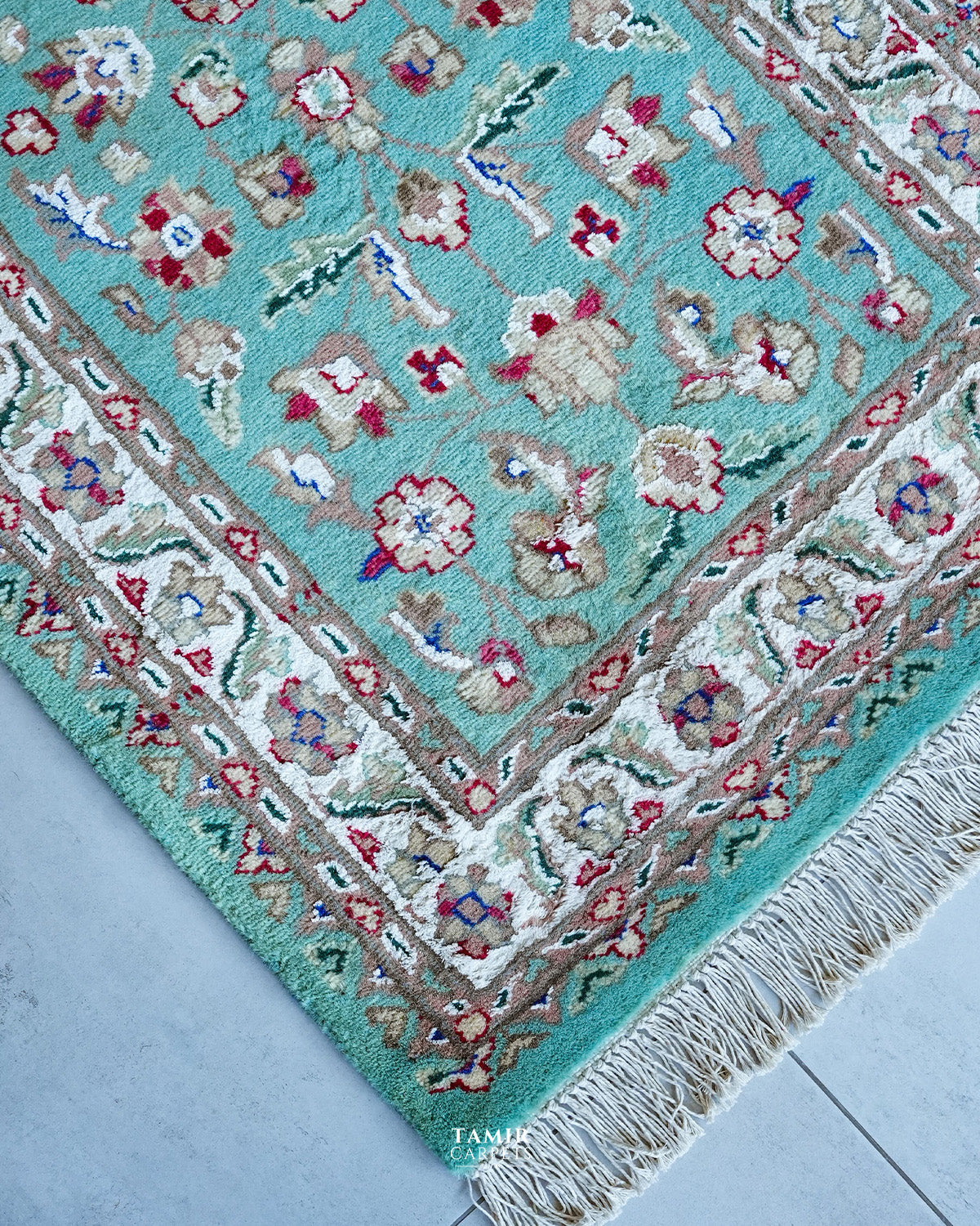 Corner of the aqua runner showing the ivory floral border and fringe