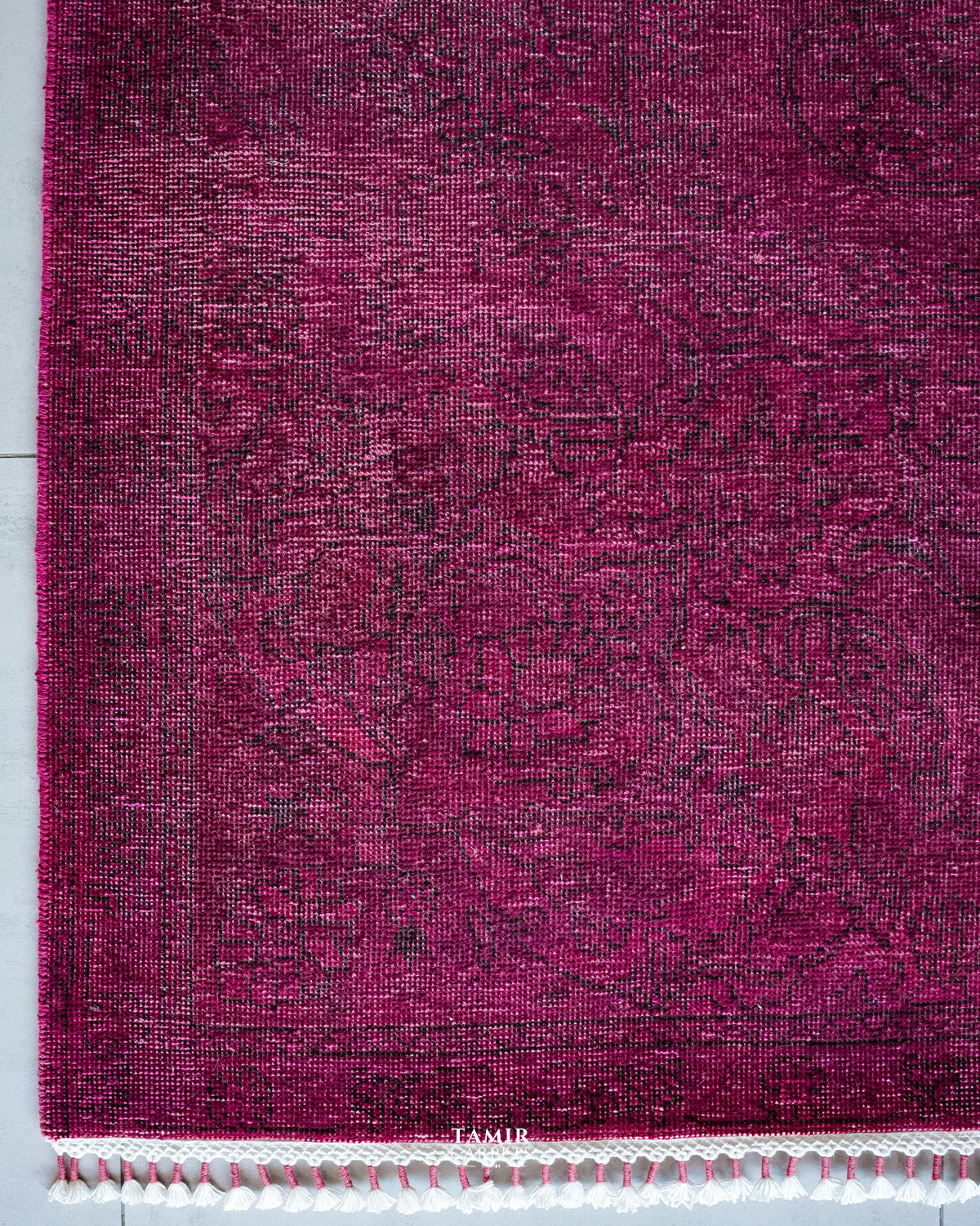 Corner of the magenta overdyed rug with faded vintage pattern and fringe