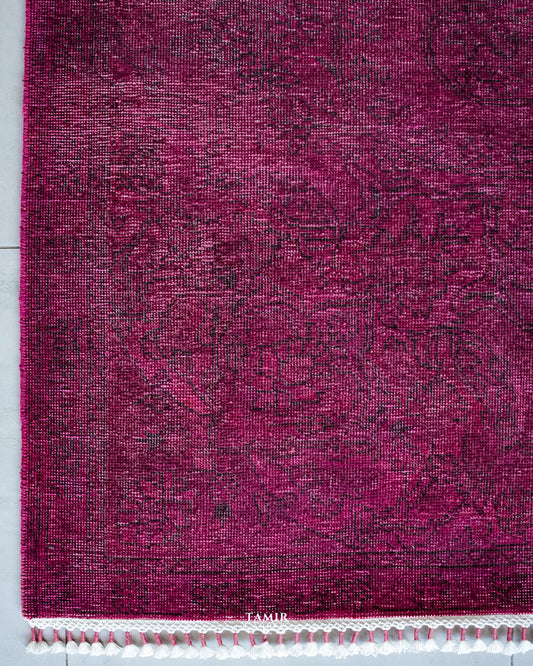 Corner of the magenta overdyed rug with faded vintage pattern and fringe